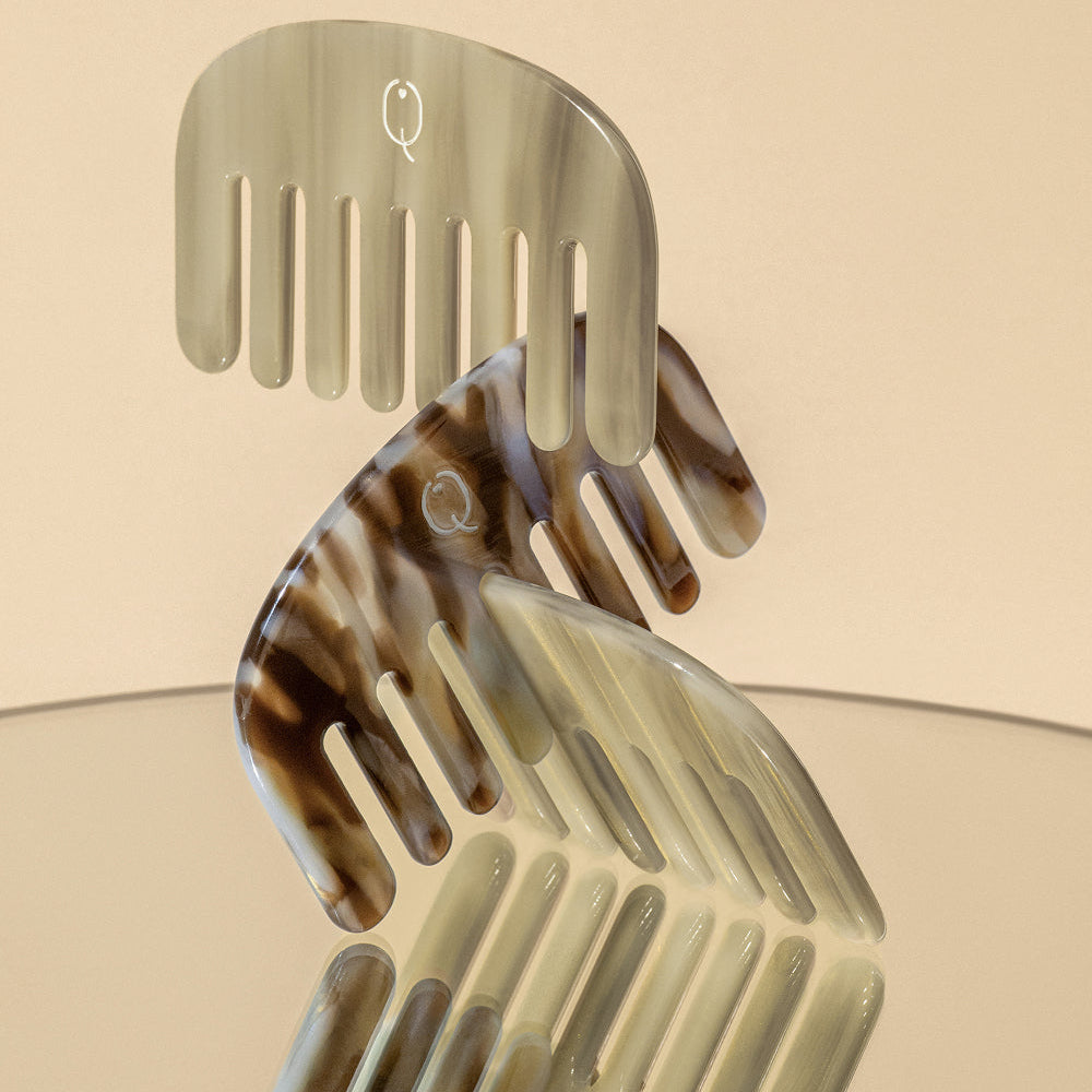 Three tortoiseshell hair combs with a glossy finish, displayed on a clear glass surface against a warm beige background.