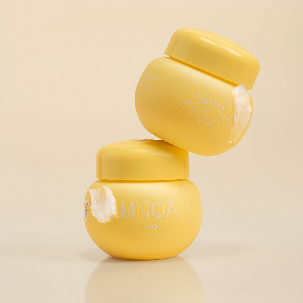 Two yellow cosmetic cream jars stacked in a balanced pyramid on a reflective beige surface, with a soft shadow beneath them.